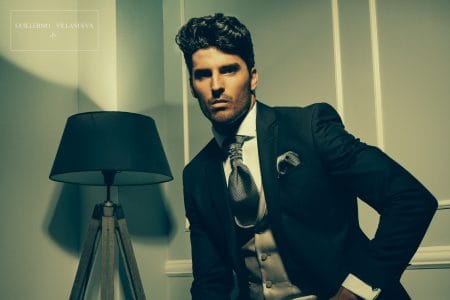 tiendas de trajes de novio Guillermo Villanueva. Traje de novio negro confeccionado con discreto tejido brocado coordinado con chaleco cuello esmoquin en color beig y corbatón en tejido de pata de gallo
