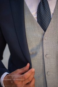Chaqué corto con levita en azul noche de ojo de perdiz coordinado con pantalón y chaleco en lino de principe de gales azul con corbata en azul con lluvia blanca, trajes de novio Guillermo Villanueva España, chalecos de novio 2026
